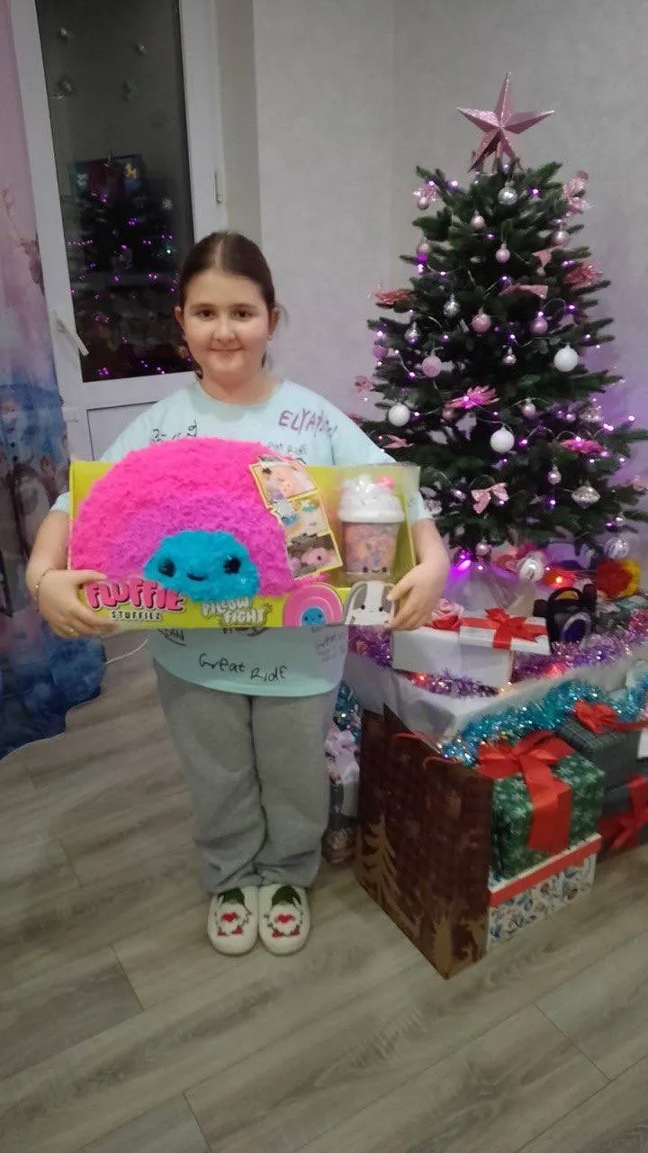 Девочка держит мягкую игрушку Fluffie Stuffiez у розовой новогодней ёлки