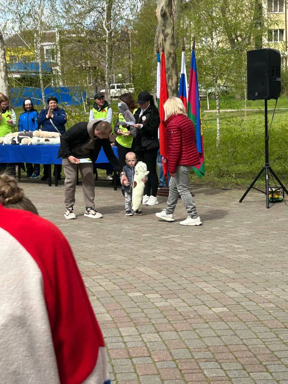 Маленький ребёнок с плюшевой нерпой в руках принимает подарок на спортивном мероприятии